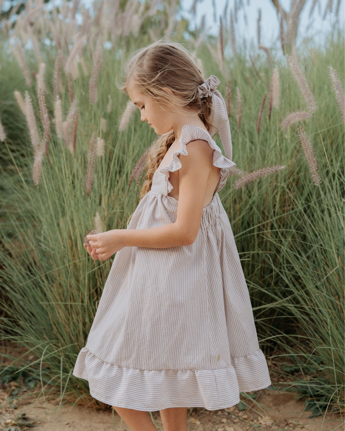 Girl model wearing the River Dress in Striped Beige and White Seersucker.