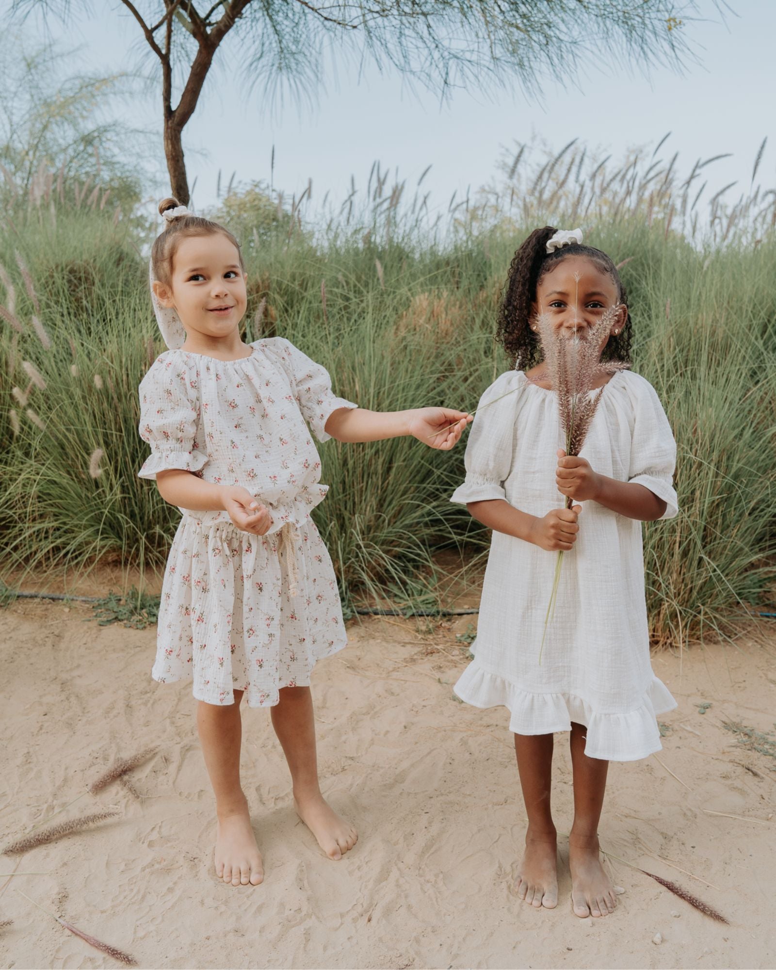 Girl model on the left wearing the Alexa Top, Sienna Skirt and Scrunchie Long in Wildflower Muslin Cottom. Girl model on the right wearing the Alexa Dress in White Baby Cotton Linen.
