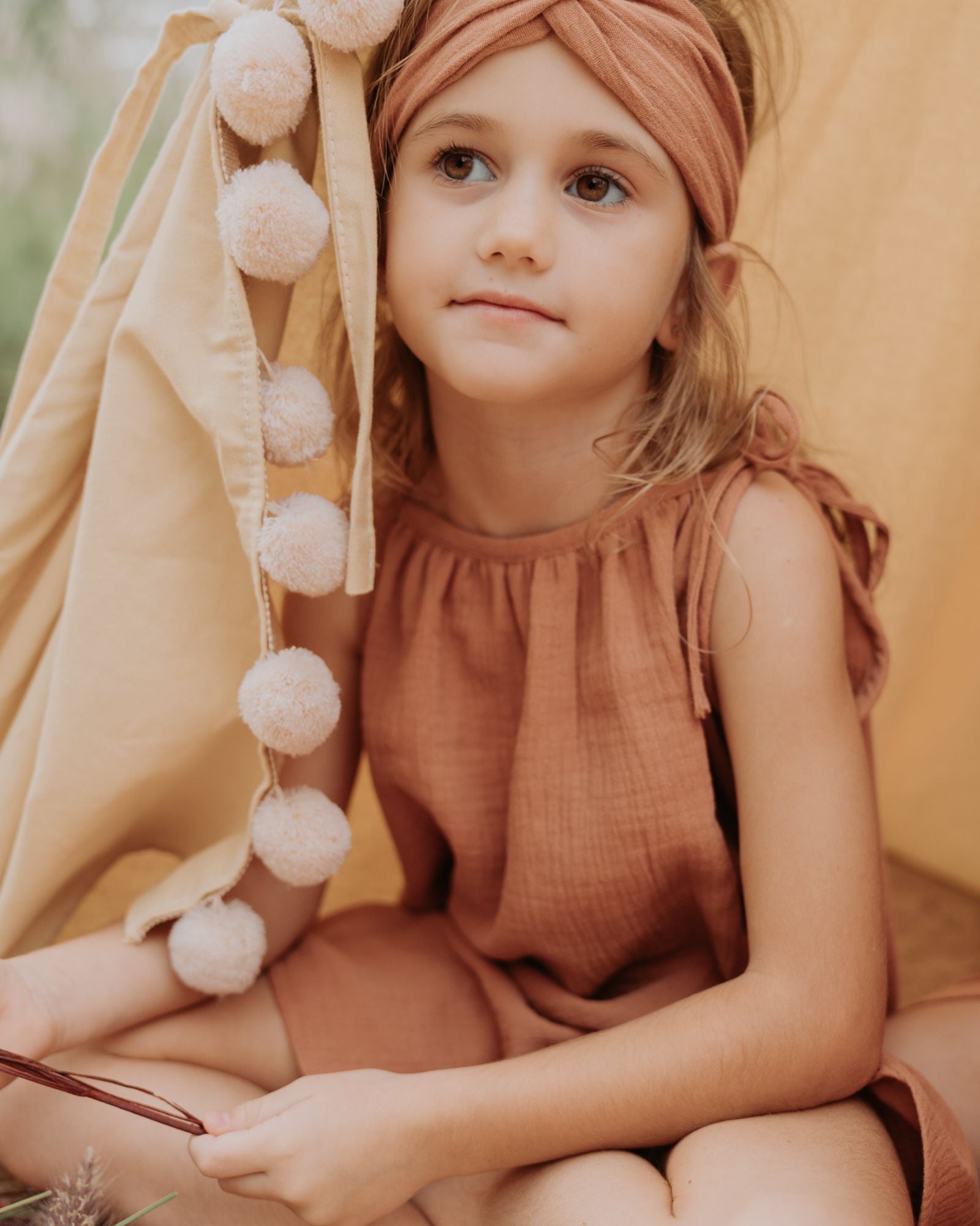 Girl model wearing the Twisted Headband in Caramel with the matching Romy Dress in Caramel.