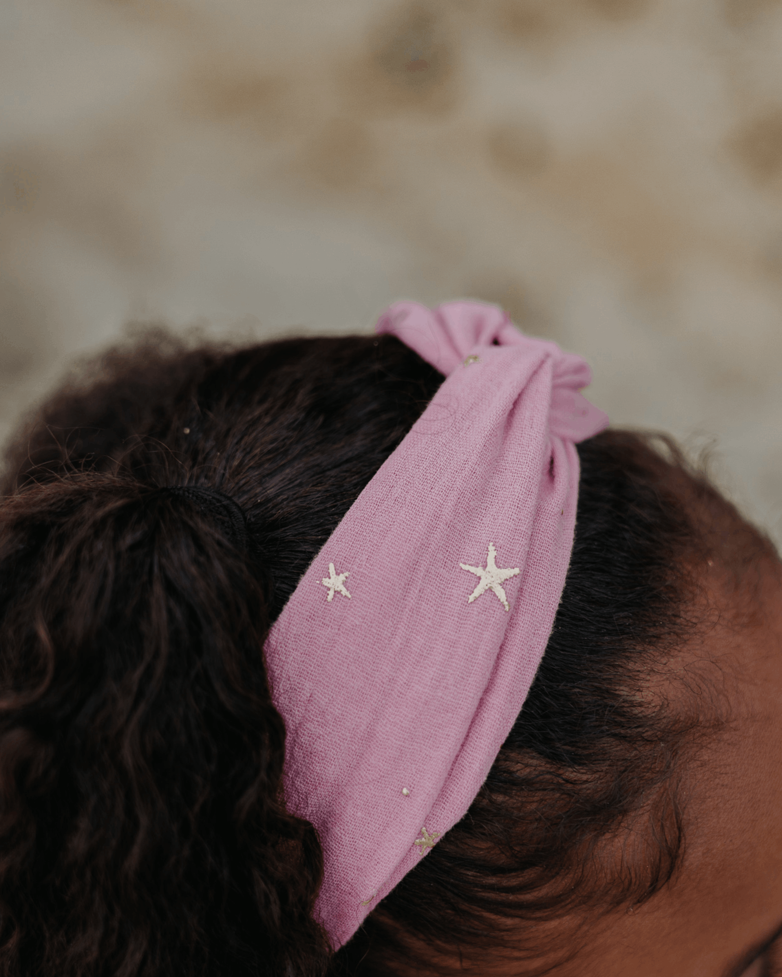 Girl model wearing the Twisted Headband in Rose Pink with Drop Stars Gold.