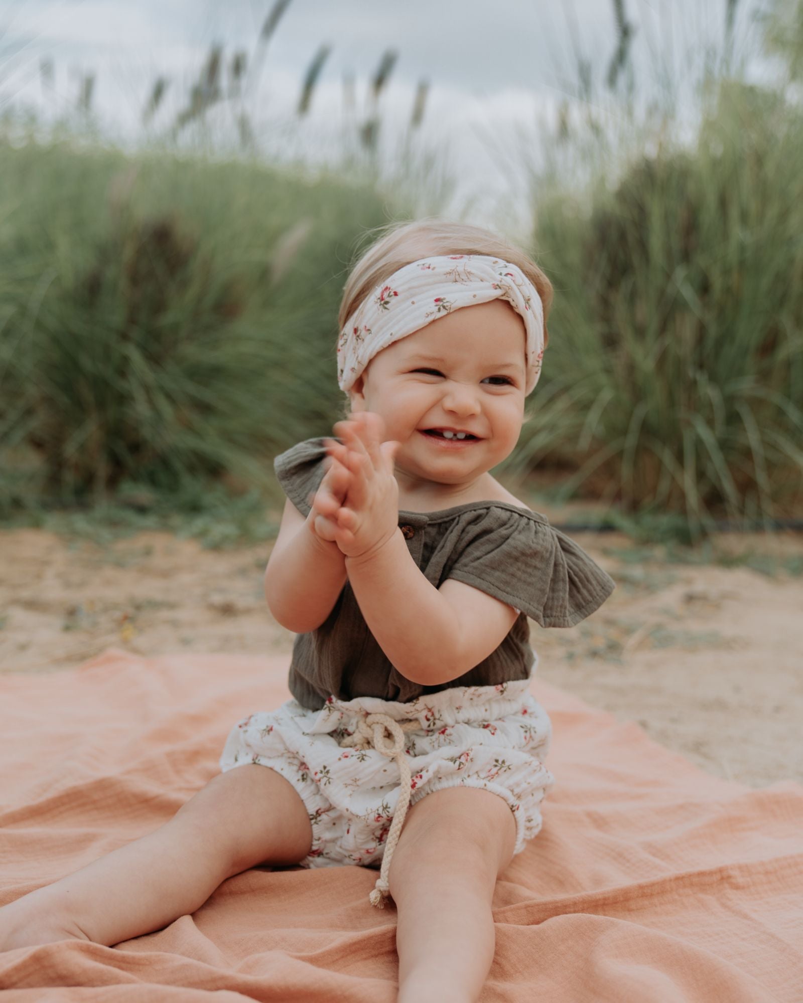 baby girl model wearing the Lilou shirt in soft khaki green muslin cotton with the bloomers in wildflower muslin cotton, combined with the twisted headband in wildflower muslin cotton