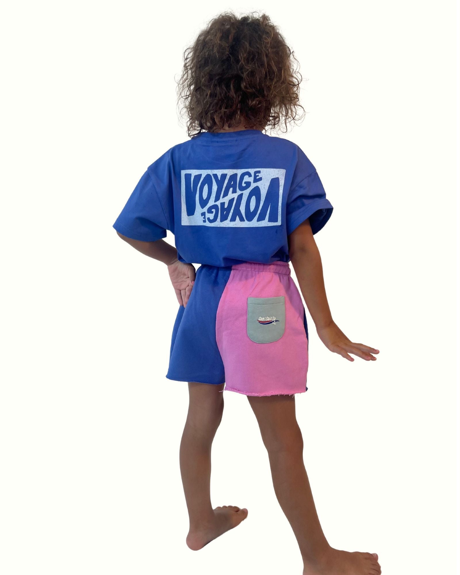 girl model showing the color block shorts with matching unisex t-shirt voyage in ultramarine blue from the back