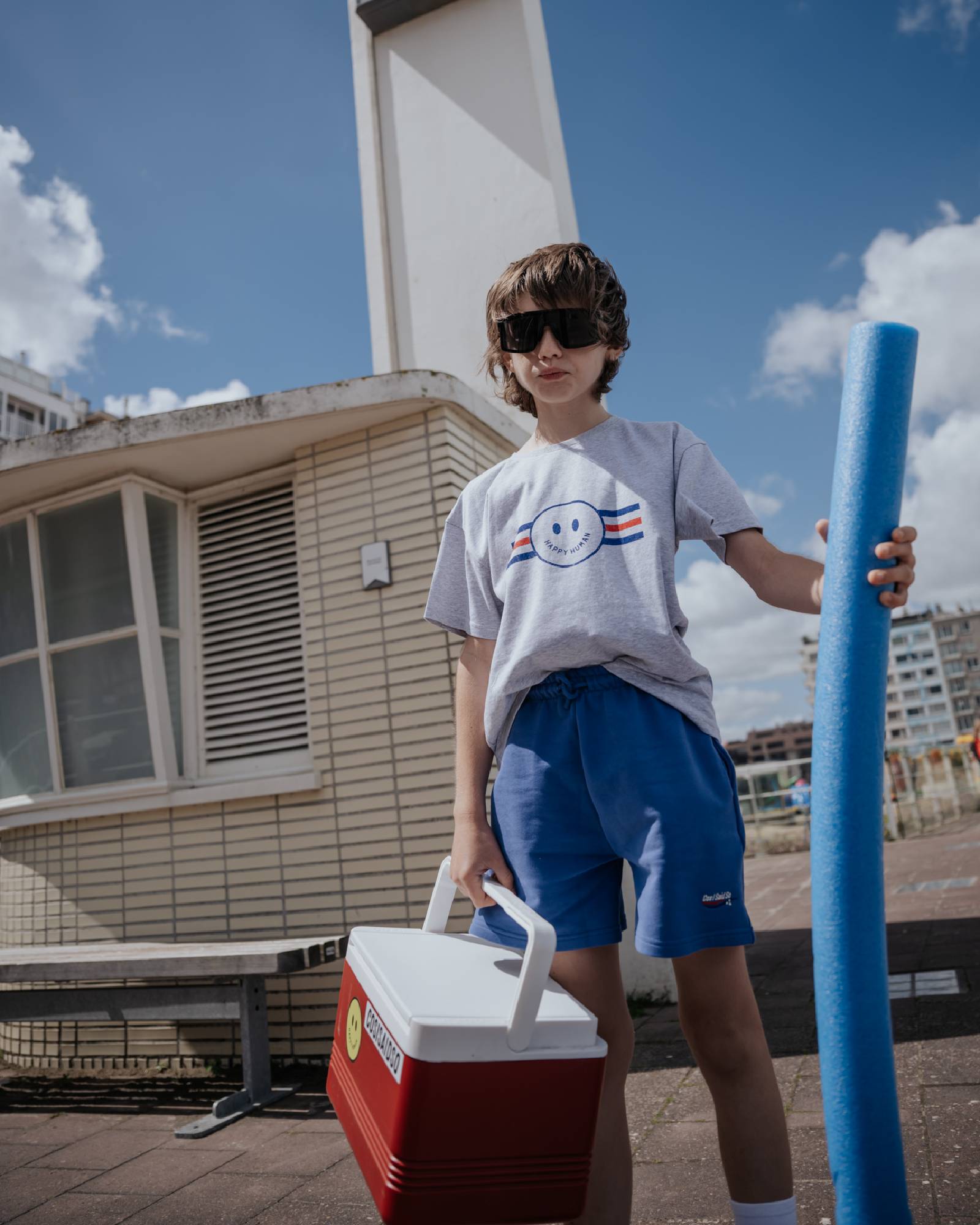 boy model wearing the jog shorts in ultramarine blue with the happy human smiley t-shirt in grey melange