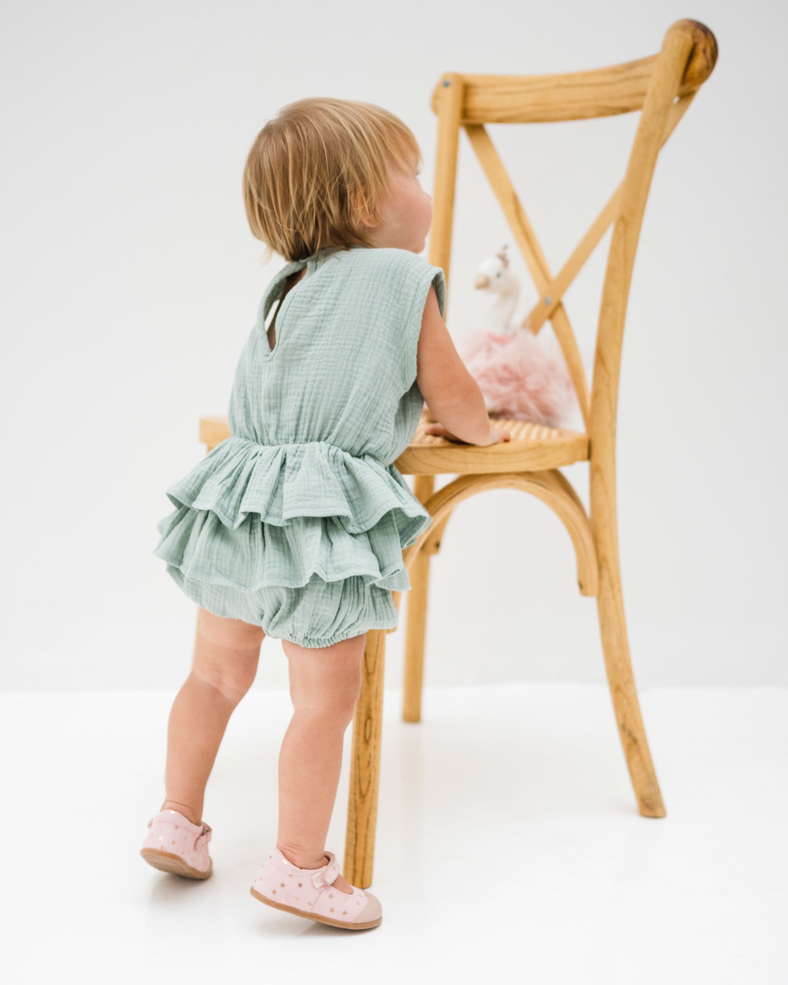 baby girl of 12 months is wearing the lina onesie in sage green in soft organic muslin cotton, showing the back