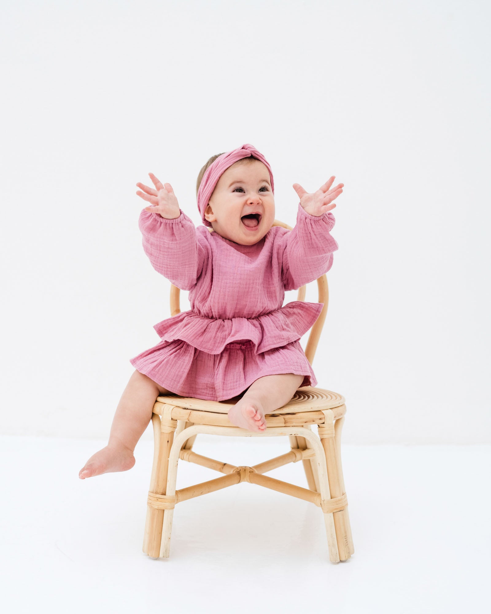 happy baby girl wearing the helena onesie in blush pink muslin with long sleeves and the matching twisted headband