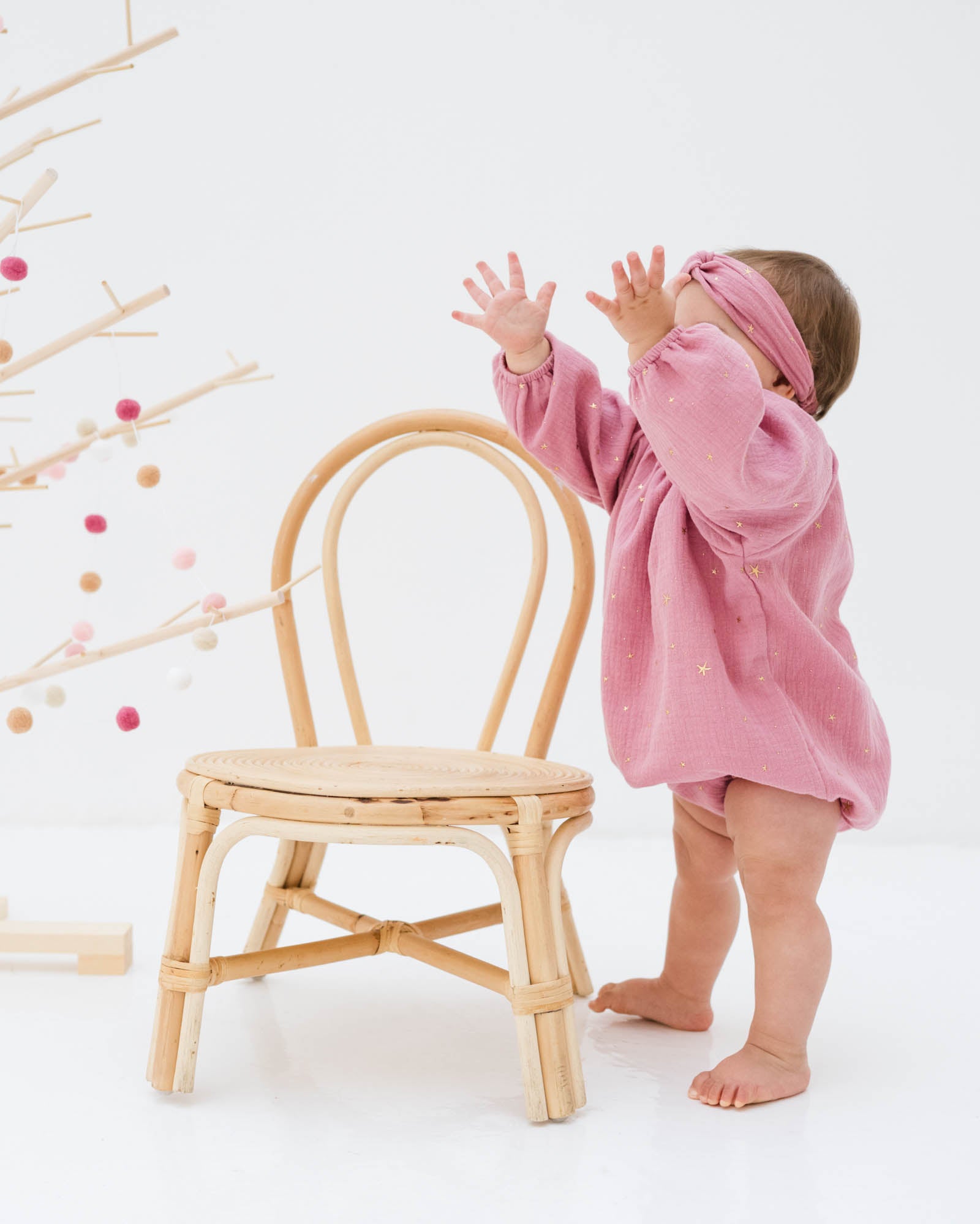 baby girl wearing the Romane onesie in rose pink with golden drop stars and the matching twisted headband