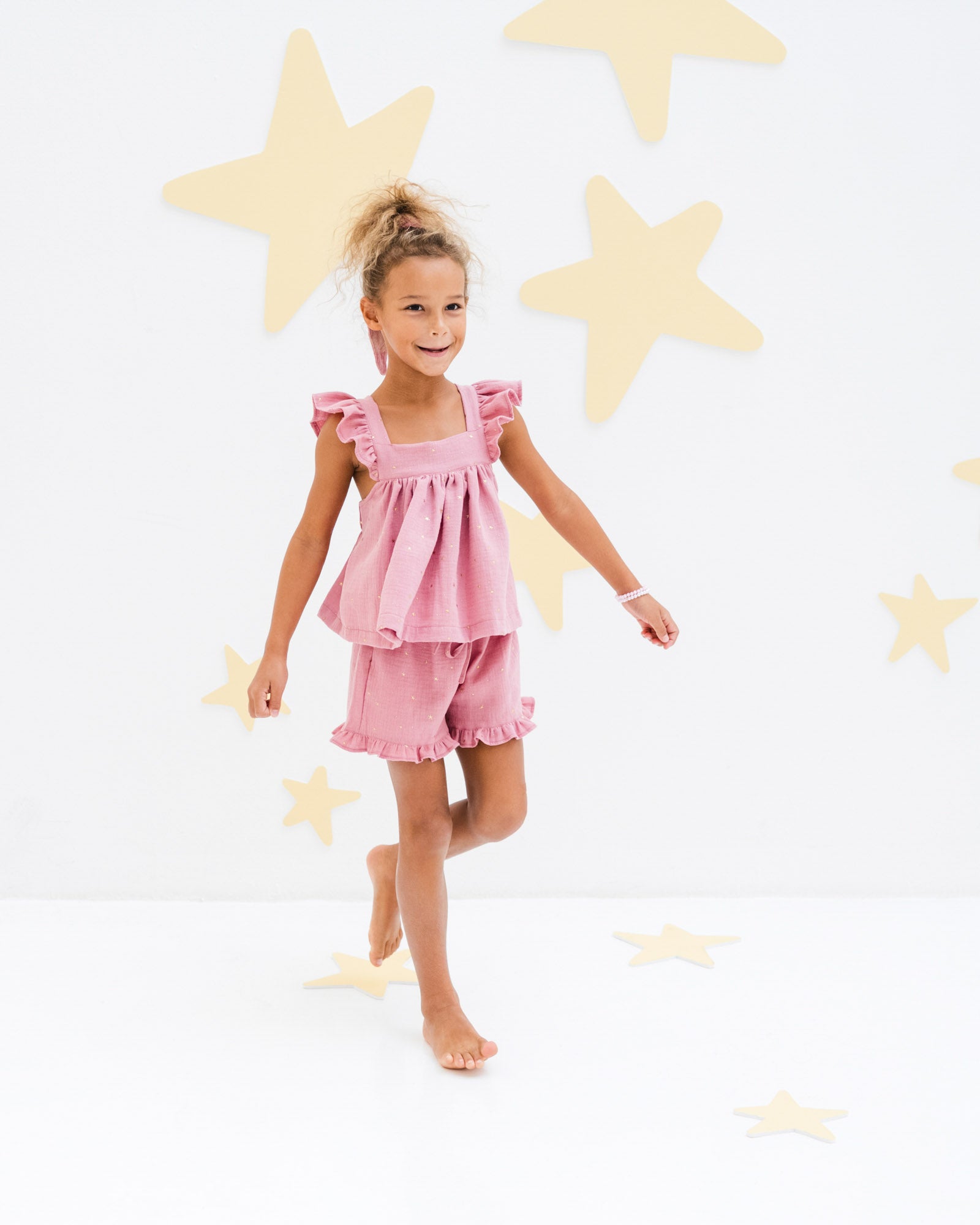 7-year-old-girl showing the frilled charlene shorts in rose pink with golden stars from the side with the frilled rosalie top