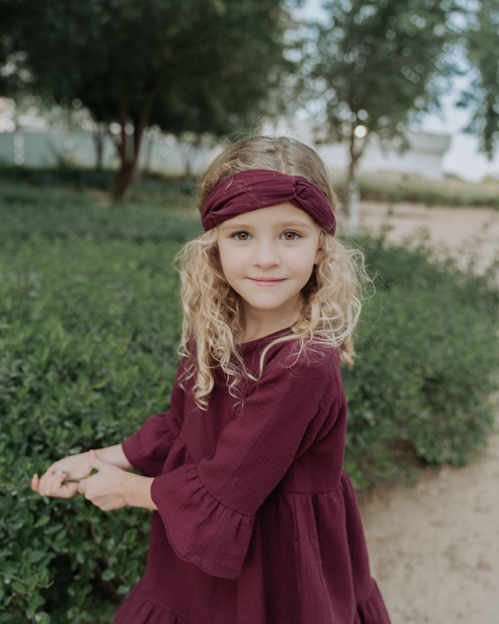 girl model wearing the twisted headband in aubergine muslin cotton and the Penelope dress in aubergine muslin cotton