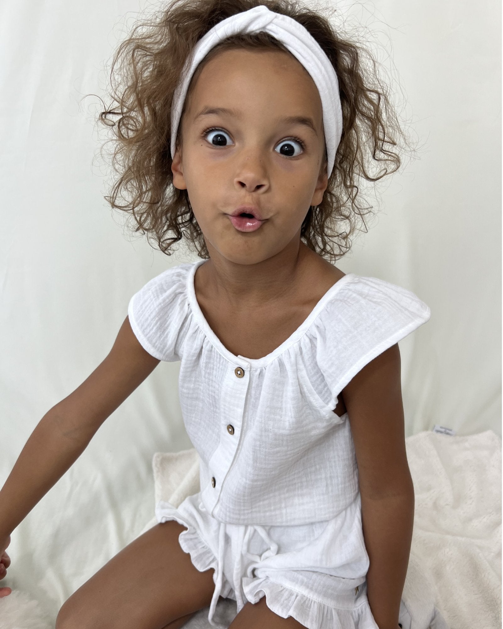 girl model wearing the twisted headband in white, the lilou blouse in white and the charlene shorts in white