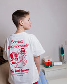 Boy wearing the white Good Vibes kids T-shirt by Cos I Said So, back view