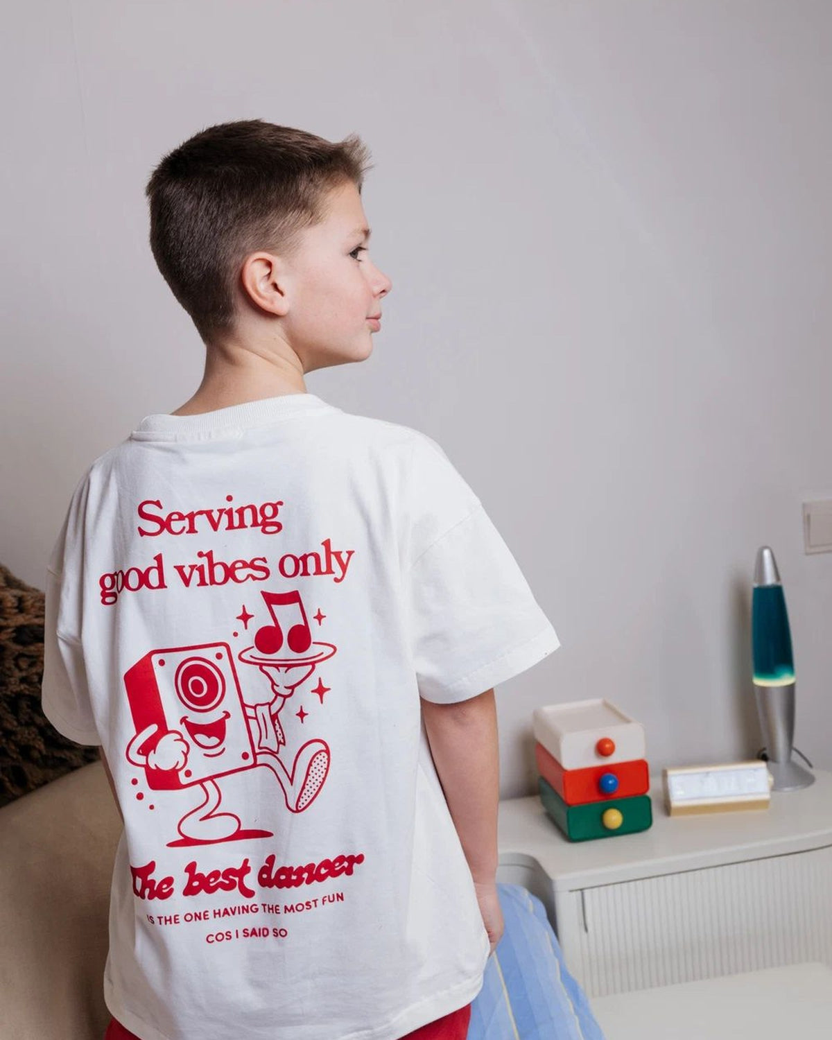 Boy wearing the white Good Vibes kids T-shirt by Cos I Said So, back view