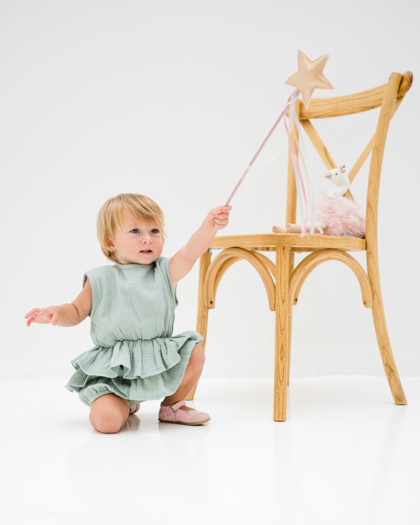 baby girl of 12 months is wearing the lina onesie in sage green in soft organic muslin  cotton