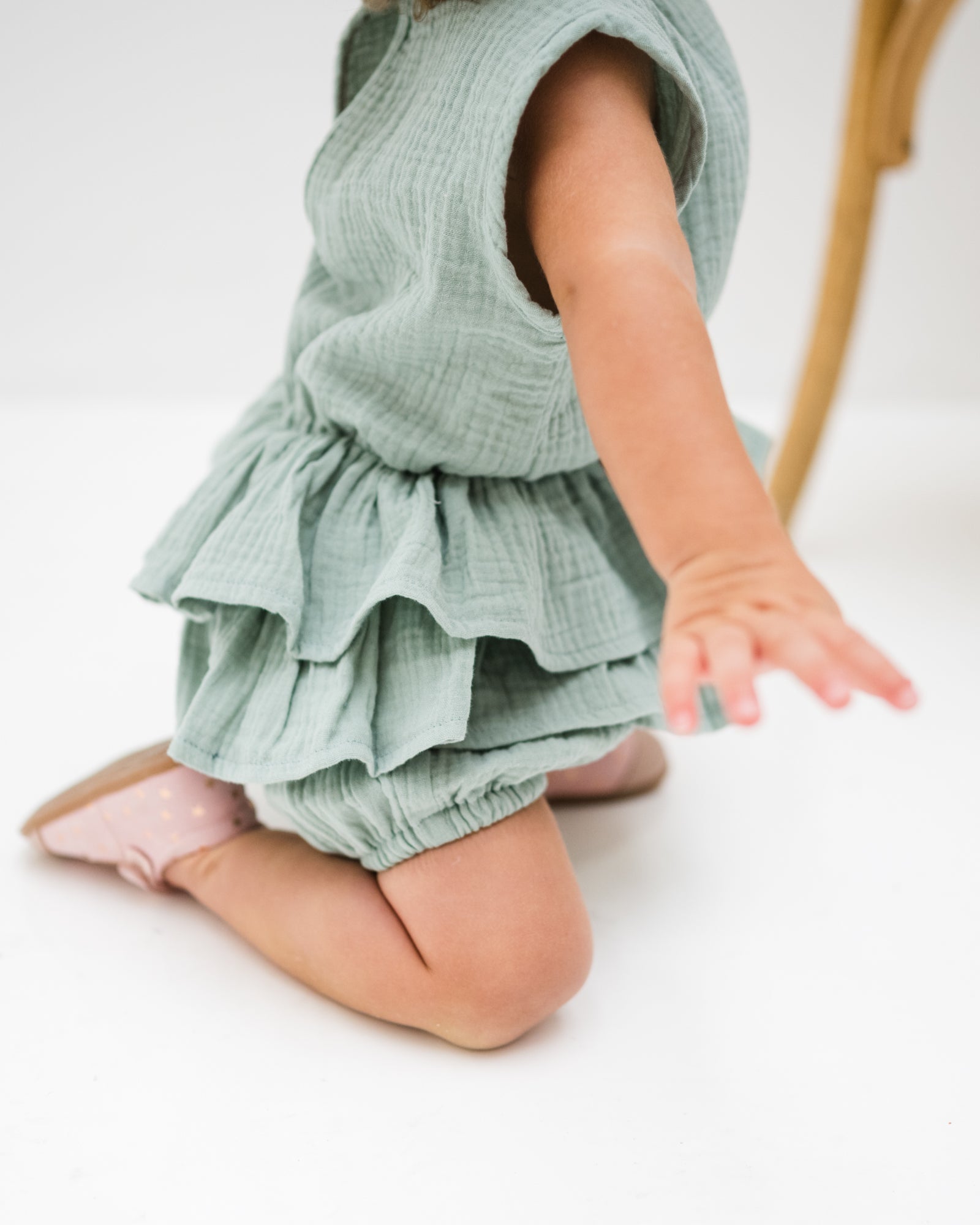 baby girl of 12 months is wearing the lina onesie in sage green in soft organic muslin  cotton, showing the side