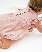 baby girl of 12 months showing the frilled Rose romper in soft pink muslin from the  back