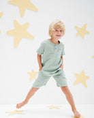  boy model wearing the charlie shirt combined with the julian shorts in sage green soft organic muslin cotton
