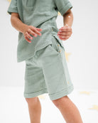 boy model is wearing the julian shorts in sage green in soft organic muslin cotton