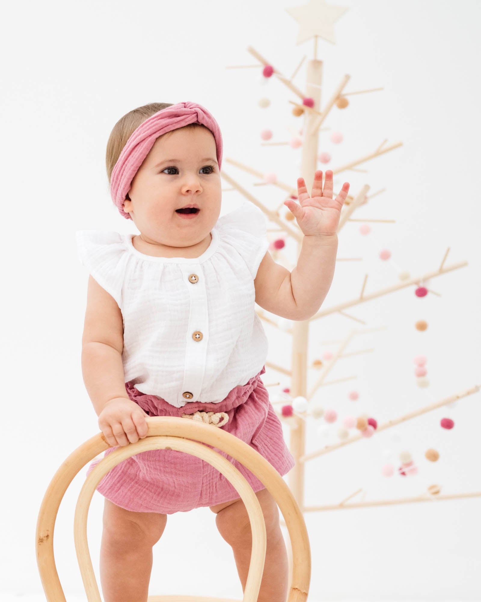 baby girl wearing the lilou top in white muslin with chlochlo bloomer in blush pink and the matching twisted headband