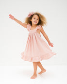 girl model wearing the river dress in soft pink muslin cotton. the dress has volume, frilled straps and frilled hem at the bottom