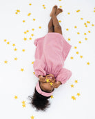 sassy 2-year-old girl laying on the floor between stars, wearing the romane dress with long sleeves in rose muslin cotton with golden stars