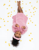 2-year-old girl laying on the floor between stars, wearing the comfortable and stylish romane dress with long sleeves in rose muslin cotton with golden stars