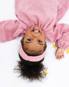 sassy 2-year-old girl laying on the floor between stars, wearing the romane dress with long sleeves in rose muslin cotton with golden stars, showing her tongue