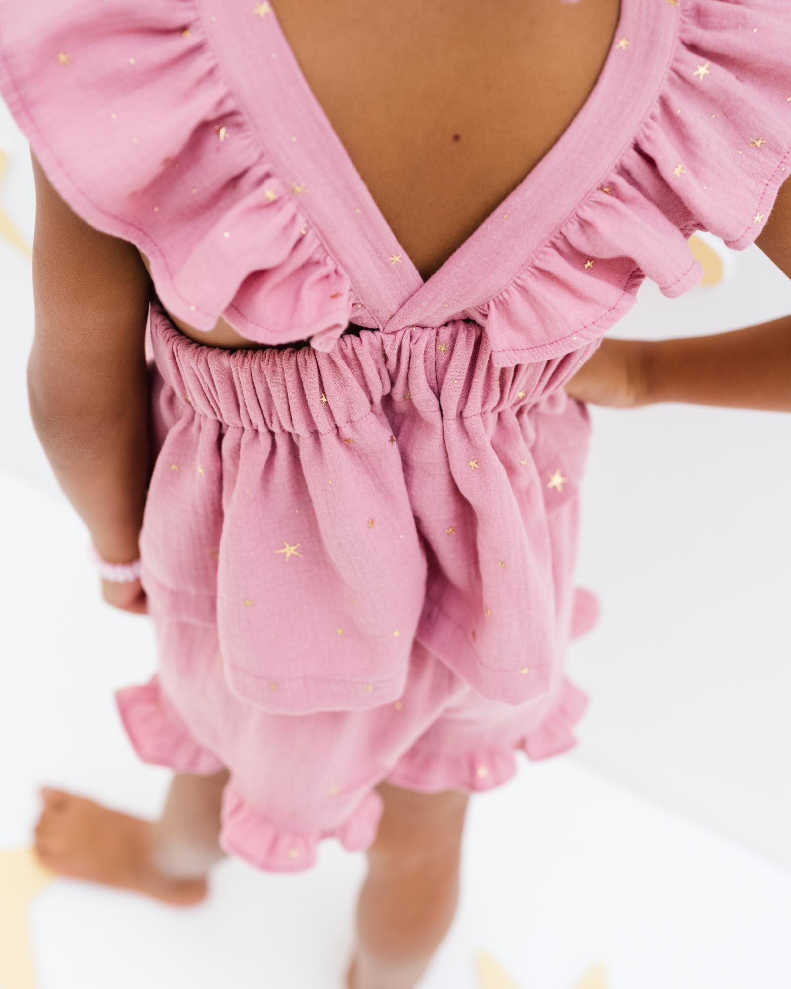 girl model showing the back of the frilled Rosalie top in rose pink muslin cotton with golden stars and matching Charlene shorts with a frilled hem