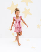 7-year-old girl model wearing the frilled Rosalie top with the frilled Charlene shorts in rose pink with golden stars
