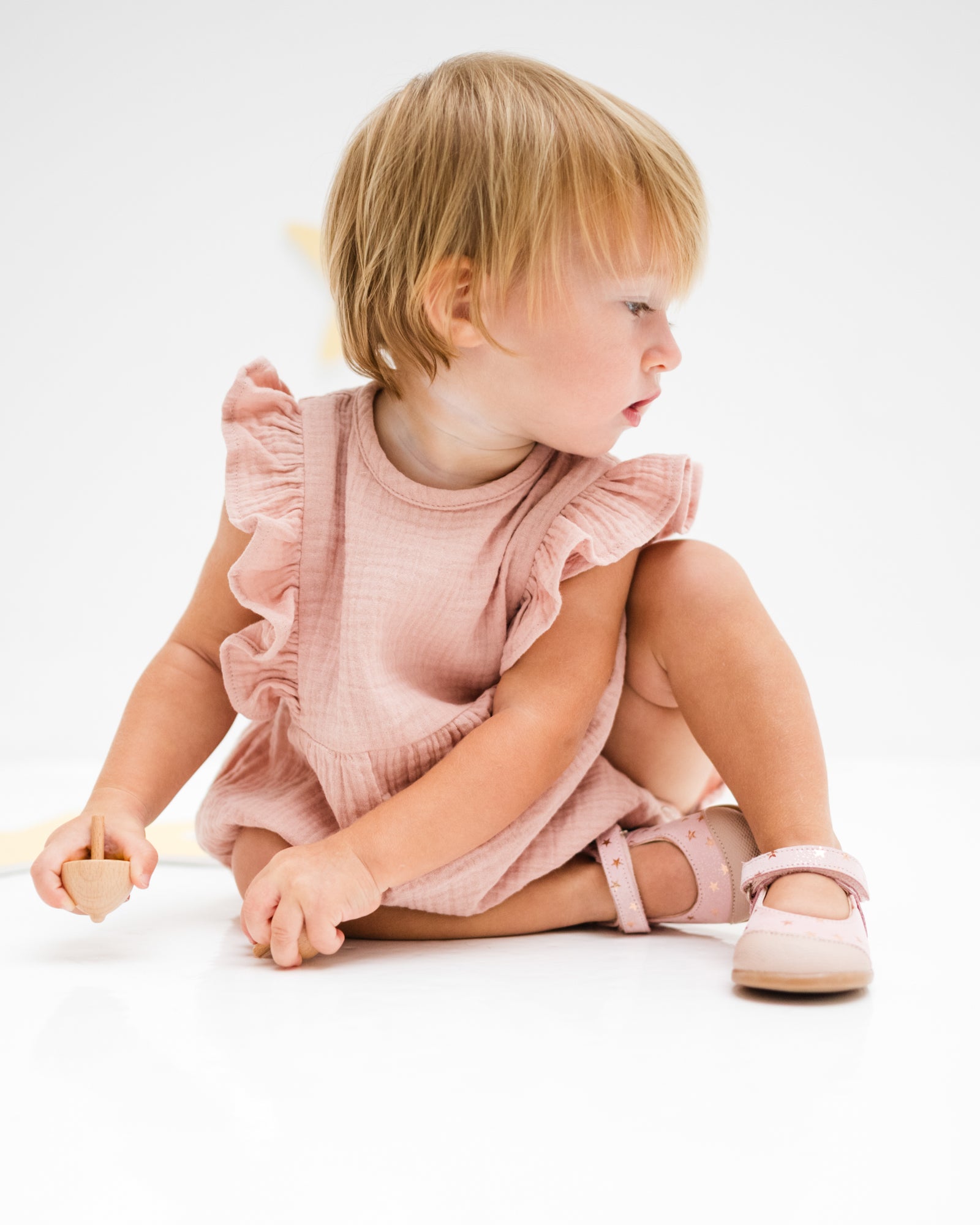 baby girl of 12 months showing the frilled Rose romper in soft pink muslin from the  back
